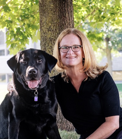 a portrait of Stephanie and Tucker the Service Dog, on a grassy spot under a tree.